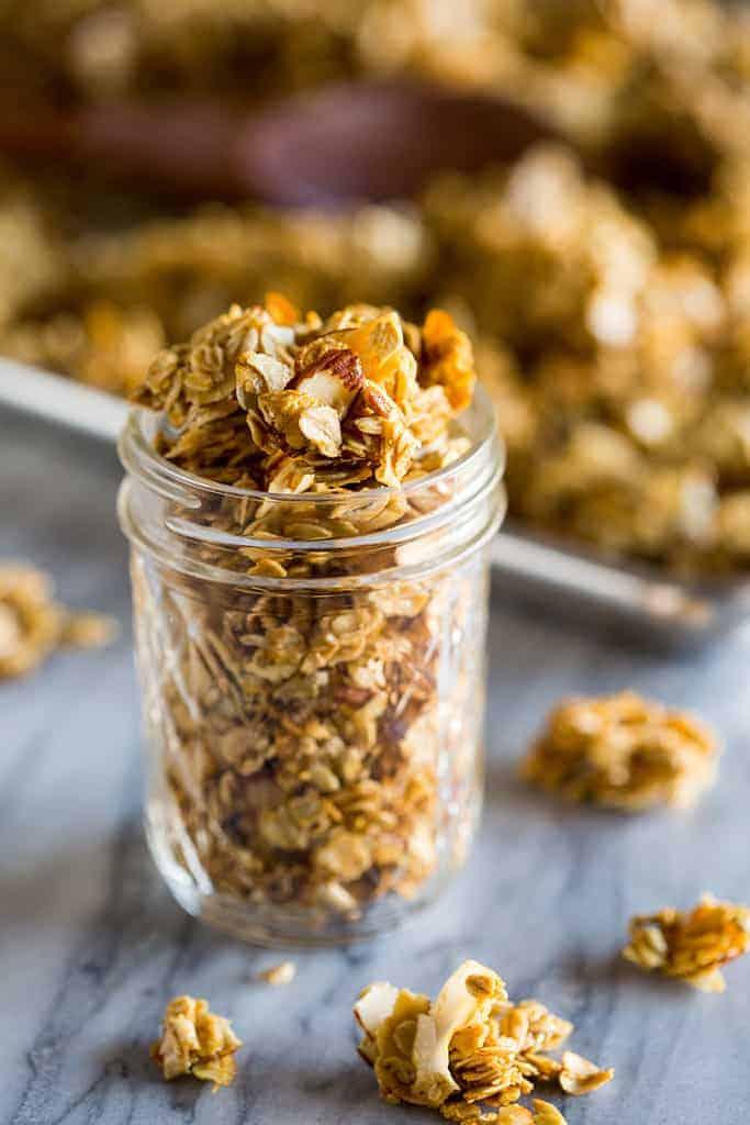 A mason jar filled with homemade granola and a sheet pan of baked granola in the background.