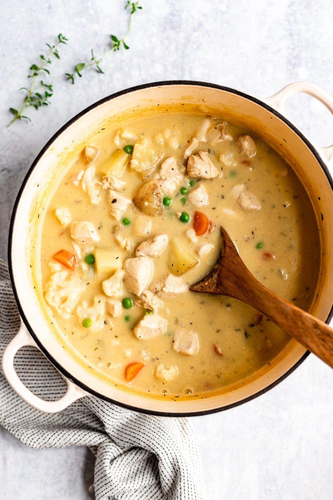 chicken pot pie soup in a pot with a wooden spoon