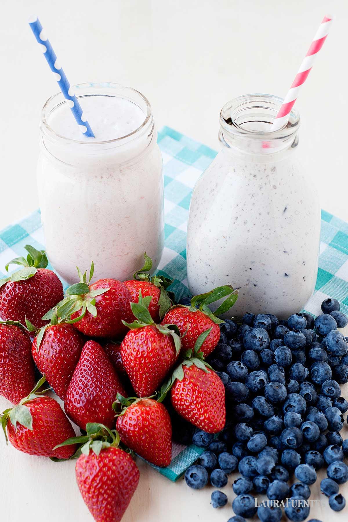 homemade yogurts in glass jars with strawberries and blueberries in front of them